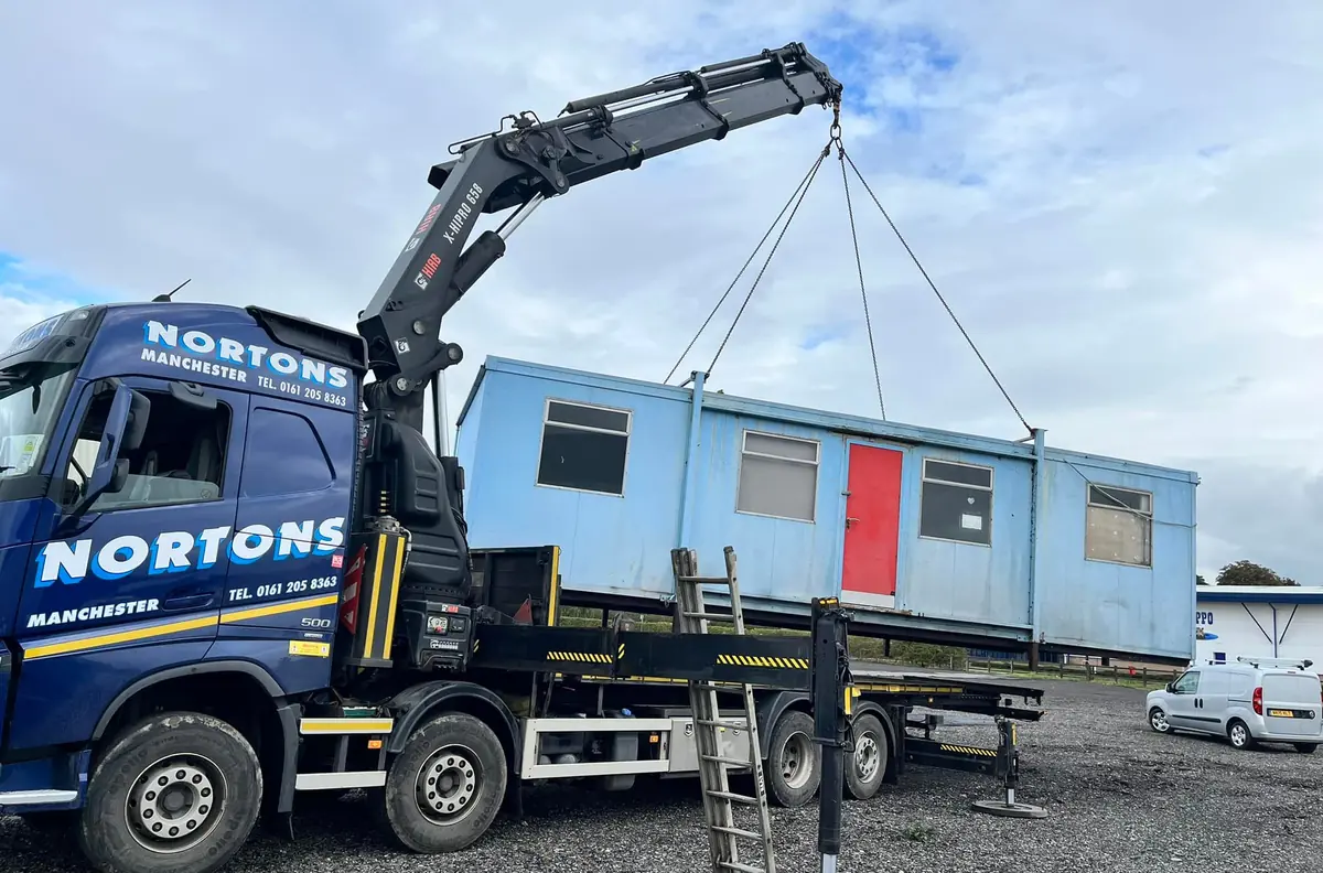 Hiab lorry lifting a used portable cabin off a construction site