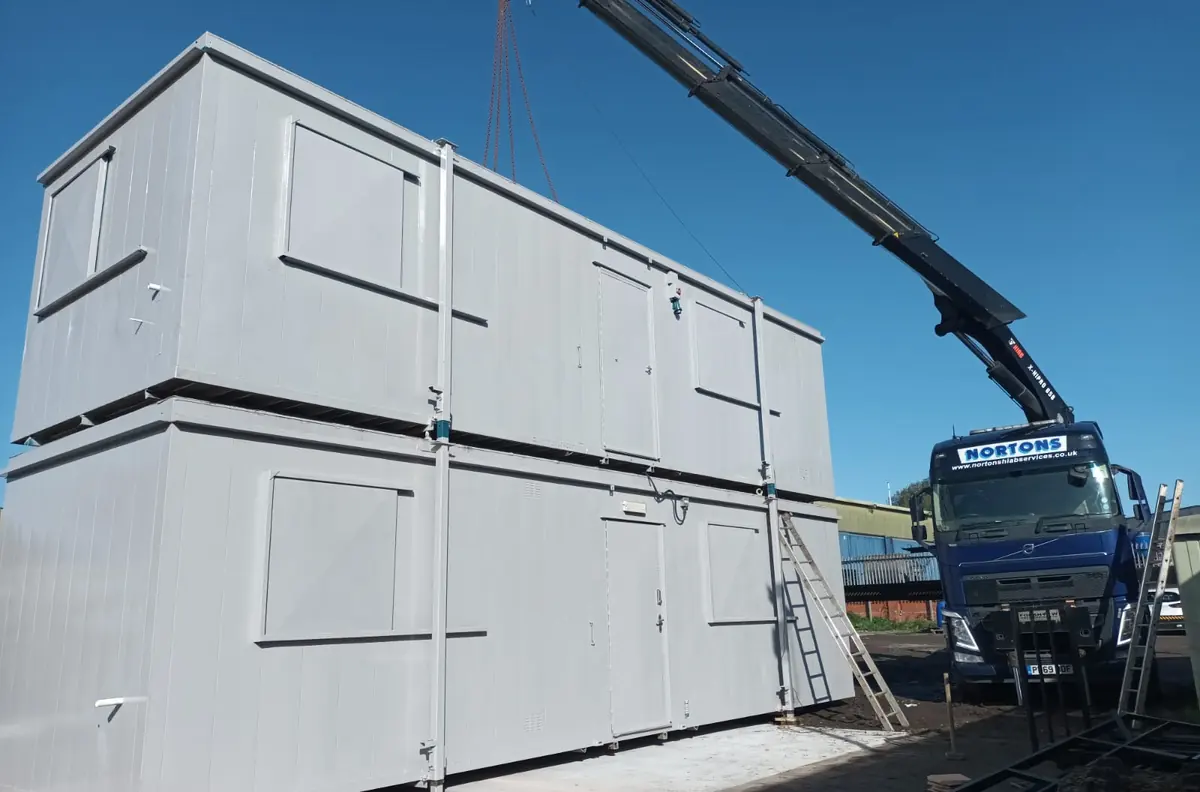 Hiab crane lifting a used portable cabin clear of the ground on a hard standing